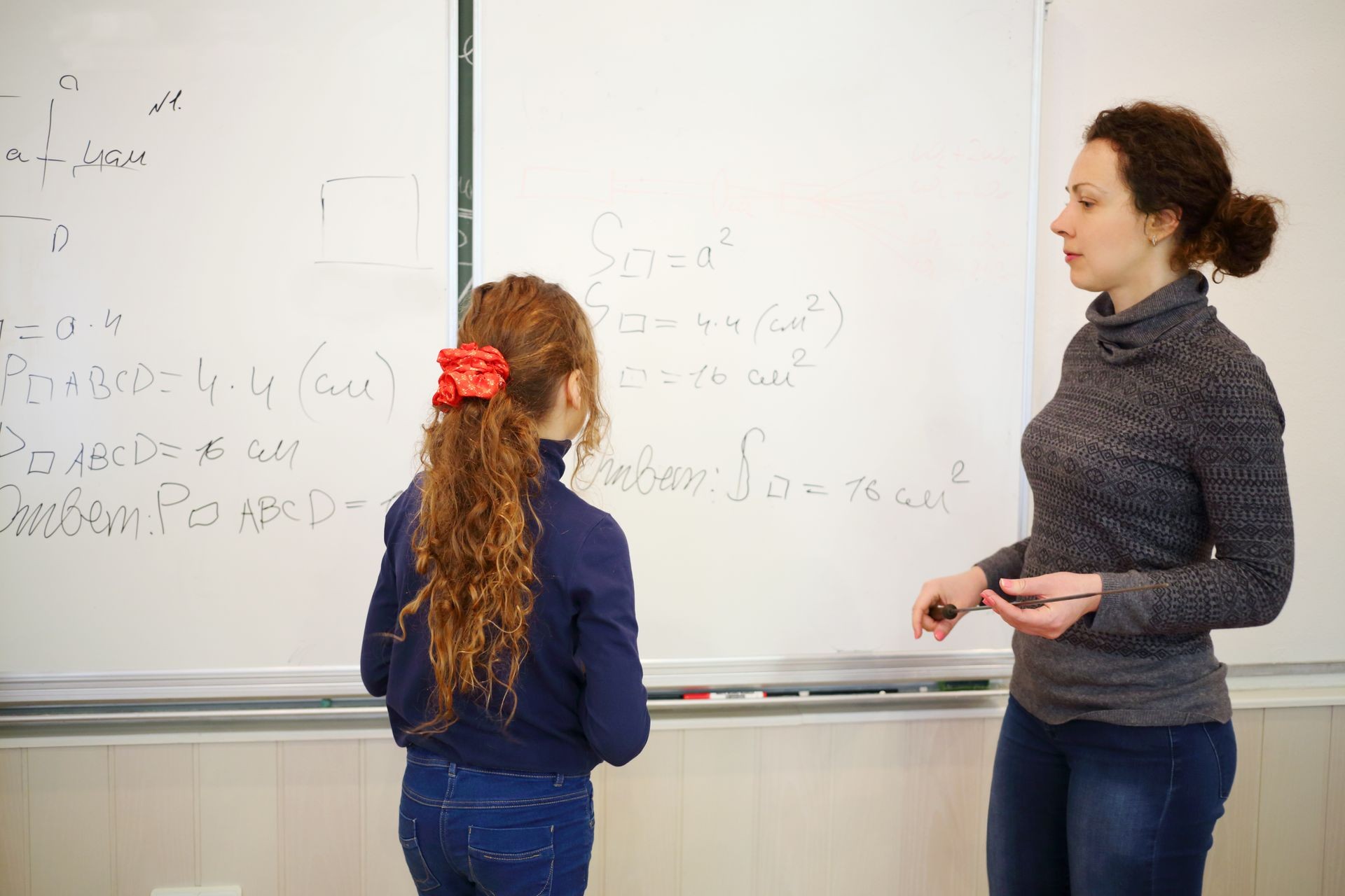 Schoolgirl and teather stand near blackboard with geometry example in classroom, text - solution, focus on child